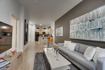 A modern living room with a grey couch and a large abstract painting on the wall.